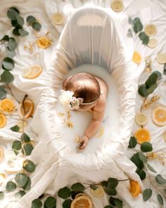 an overhead view of a baby laying in a bathtub surrounded by oranges and leaves