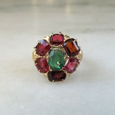 This is an antique Art Deco 1920s multi-gemstone ring.  There is an oval emerald in the center surrounded by 2 garnets & 4 rubies.  All of the rubies have a small chip out of it except for one.  One has a piece missing around it's table.  Both garnets have a very small chip.  The ring face measures 14mm in diameter.  The band is sized at 4.  Total weight of the ring is 3.9 grams. This is an antique, previously owned ring.  Light antique wear can be expected. Antique Multi-stone Round Emerald Ring, Antique Round Multi-stone Emerald Ring, Vintage Multi-stone Oval Cabochon Rings, Vintage Multi-stone Emerald Ring, Vintage Multi-stone Round Emerald Ring, Vintage Multi-stone Ruby Cluster Ring, Vintage Multi-stone Ruby Ring, Vintage Ruby Multi-stone Cluster Ring, Vintage Ruby Cluster Ring With Multi-stones