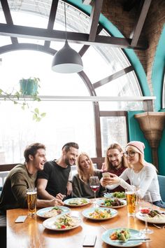 group of people sitting around a table with food and drinks in front of them smiling at the camera