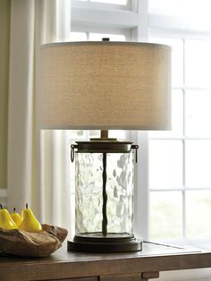 a table lamp sitting on top of a wooden table next to a basket of fruit