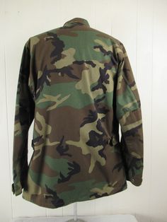 "Vintage 1980s camouflage U.S. Air Force military jacket. Made of green camo Nylon/cotton. Has U.S. Air Force patch, a button front, button cuffs, four pockets and button side cinches. Size medium long. Actual measurements are: 47\" at the chest 44\" at the waist 18\" shoulder seam to shoulder seam 26.5\" shoulder seam to end of cuff 33.5\" overall length. In excellent condition." Combat Cotton Camouflage Outerwear, Military Camouflage Windbreaker For Fall, Camouflage Cotton Combat Outerwear, Combat Style Camouflage Cotton Outerwear, Camouflage Cotton Utility Jacket For Outdoor, Military Style Camouflage Cotton Outerwear, Air Force Jacket, 1980s Jacket, Air Force Patches