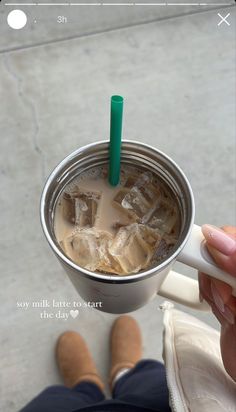 a person holding a cup with ice in it and a green straw sticking out of the top