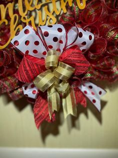 a red and white christmas wreath with gold bow on it's side, next to a welcome sign