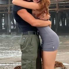 a man and woman hugging each other on the beach with water in the back ground