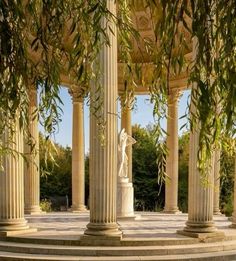 an outdoor gazebo with columns and statues surrounded by trees