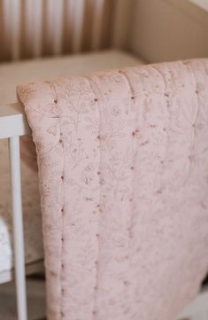 a baby crib with a pink blanket on it and a white chair next to it