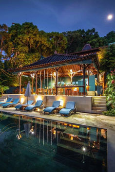 an outdoor swimming pool with lounge chairs next to it and trees in the background at night