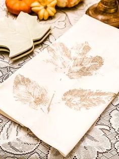 a table topped with plates and napkins covered in fall leaves on top of a doily