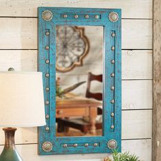 a blue framed mirror sitting on top of a table next to a lamp and vase