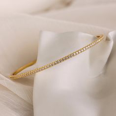 Our Classic Diamond Tennis Bangle is a dainty gold piece adorned with sparkling pavé stones, exuding elegance and sophistication. Perfect for any occasion, this versatile bracelet can be worn alone for a subtle touch of glamour or stacked with other bracelets for a classy, layered look ♡ SKU: RR-BR065 Product Details Material: 18K Gold Over Brass Finish: 18K Gold Featuring ~2.5mm wide Diamond Bangle Bracelet with CZ Pavé Diamond Stones Featured Styles Part of our Diamond & Pavé Collection Model Dainty Gold Bracelets With Sparkling Stones, Dainty Gold Bracelet With Sparkling Stones, Dainty Tennis Bracelet With Diamond Accents, Elegant Tarnish-resistant Tennis Bracelet For Weddings, Dainty Gold Sparkling Bracelet, Adjustable Gold Bracelet With Pave Setting, Delicate Gold Tennis Bracelet For Wedding, Gold Diamond Bracelet With Sparkling Stones For Formal Occasions, Formal Gold Diamond Bracelet With Sparkling Stones