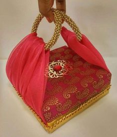 a hand holding a pink and gold purse