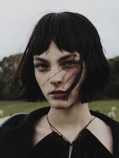 a woman with black hair and makeup looks at the camera while standing in a field