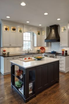 a large kitchen with an island in the center and white cabinets on both sides, surrounded by wood flooring