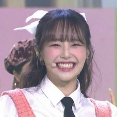 a young woman wearing a white shirt and black tie smiles at the camera while standing in front of an audience