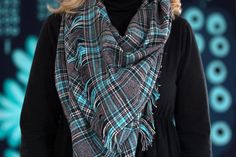 a woman wearing a black sweater and plaid scarf with the words flannel & fringe on it