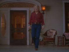 a woman in red shirt and blue pants walking into a house