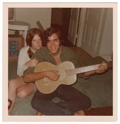 two people sitting on a bed with an acoustic guitar in their hands and one person holding the guitar