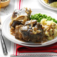 a white plate topped with meat covered in gravy next to green peas and potatoes