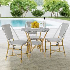 four chairs and a table with lemons on it in front of a swimming pool