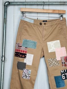 a pair of brown pants with patchwork on them hanging from a metal rack next to a white wall