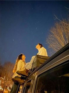 two people sitting on the roof of a car looking up at the stars in the sky