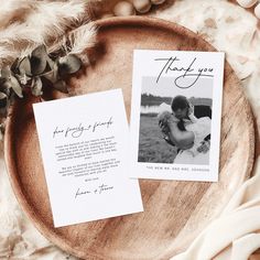 two wedding thank cards on top of a wooden plate next to some feathers and flowers