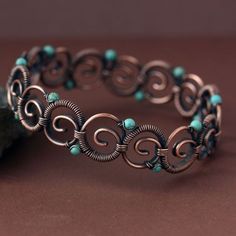 a bracelet with turquoise beads and spirals on it, sitting next to a rock