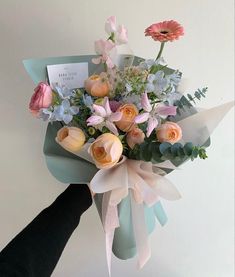 a bouquet of flowers is being held by someone's hand in front of a white wall