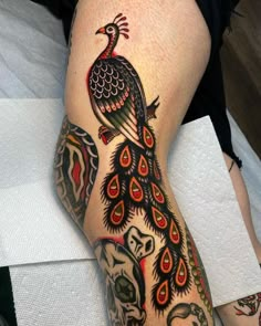 a person with a tattoo on their leg and a peacock sitting on top of it