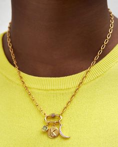 a woman wearing a yellow sweater and gold necklace with the letter c on it's side