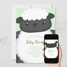 a person holding up a phone next to a baby shower card with a sheep on it