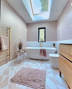 a pink bathroom with a skylight above the bathtub and rug on the floor