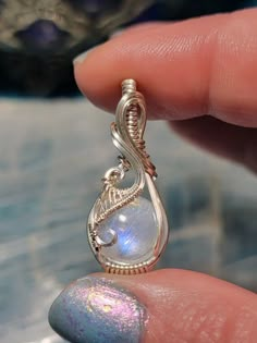 a hand holding a small silver pendant with a rainbow colored stone in it's center