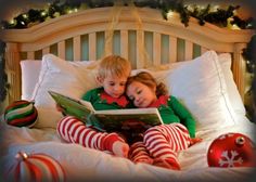 two children laying in bed with christmas decorations and reading a story book to each other