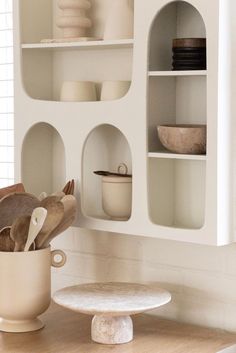 a white shelf filled with lots of dishes on top of a wooden table next to a vase