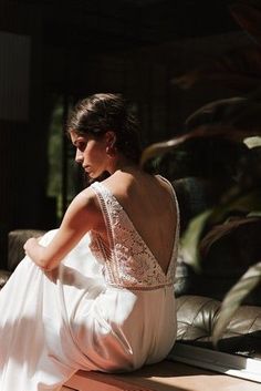 a woman sitting on top of a wooden bench in front of a window wearing a white dress