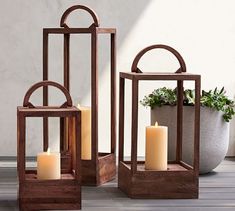 three wooden lanterns with candles in them sitting on a deck next to a potted plant