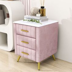 a pink and gold nightstand with books on it next to a white shelf filled with vases