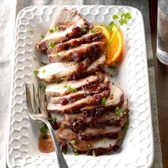 a plate with meat, oranges and sauce on it next to a glass of water