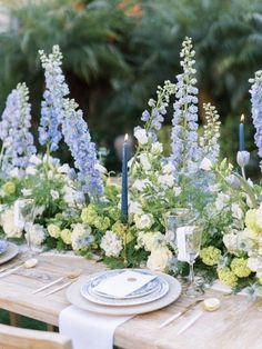 the table is set with blue and white flowers, candles, and place settings for dinner