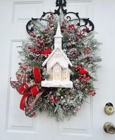 a wreath with a church on it hanging from the front door, decorated for christmas