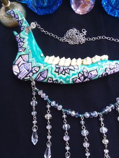 This is a Beautiful Painted,Turquoise Crystal Deer Jawbone Necklace! The Colors Here Are Just Fantastic! The Painted crystals Are a Light Purple Color And The Backdrop is Turquoise! A few rhinestones as well. Hanging from the bottom is a String of Glass beads! All 6 Teeth Are in perfect condition. The Whole Jaw Bone is 9 inches long. Also coated with polyurethane for the beautiful shine. The Chain is 20 inches long. All Items Ship Within 1-3 Days via USPS First Class Service. Shipping on This Bo Unique Handmade Bone-colored Necklace, Handmade Bone-colored Unique Necklace, Unique Handmade Bone Necklace, Bohemian Bone Colored Jewelry For Festivals, Bohemian Bone-colored Jewelry For Festival, Bohemian Bone-colored Necklace For Festivals, Painted Crystals, Real Bone Jewelry, Wiccan Necklace