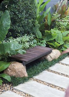 a wooden bench sitting in the middle of a garden next to some rocks and plants