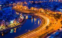 an aerial view of a city at night with lights on the streets and water in the foreground