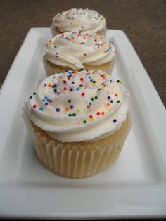 three cupcakes with white frosting and sprinkles on a plate