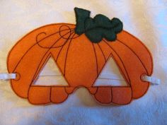 an orange felt pumpkin mask with a green bow on it's head, sitting on a white sheet