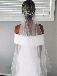 the back of a bride's wedding dress with a veil over her shoulder and beaded headpiece