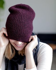 a woman wearing a knitted beanie hat with her hands on her head while looking at the camera