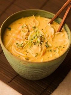 a green bowl filled with soup and chopsticks on top of a wooden mat