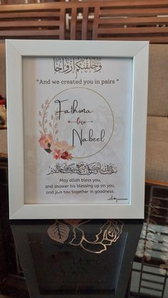 an arabic calligraphy is framed in a white frame on a table with a wooden bench behind it